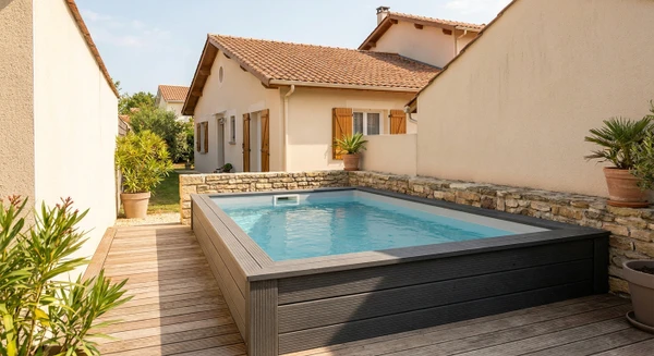 Photographie réaliste d'une mini-piscine installée dans un petit jardin ou une terrasse résidentielle, montrant une piscine compacte de forme rectangulaire ou carrée, de dimensions clairement réduites, intégrée harmonieusement dans un espace extérieur étroit ou confiné. La piscine doit être remplie d'eau cristalline et entourée d'un petit dallage ou terrasse en pierre ou bois. L'arrière-plan montre une maison résidentielle typique en Aquitaine avec un jardin de taille modérée. L'image doit illustrer la praticité et l'élégance des mini-piscines pour les espaces restreints, différenciant visuellement cette prestation des installations de piscines standards déjà représentées.